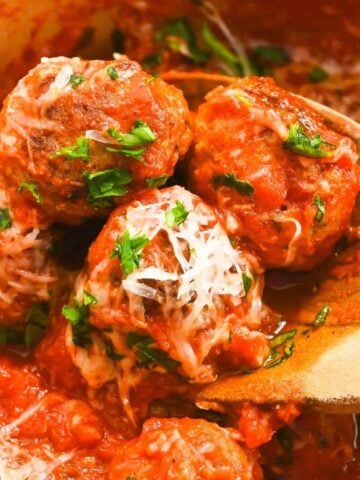 close up of eggless meatballs on a wooden spoon topped with parsley and parmesan cheese.