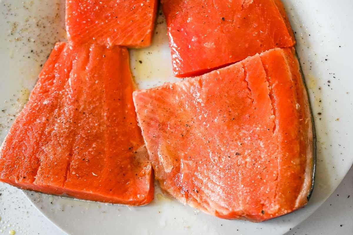salmon on a white plate seasoned with salt, pepper, and olive oil.