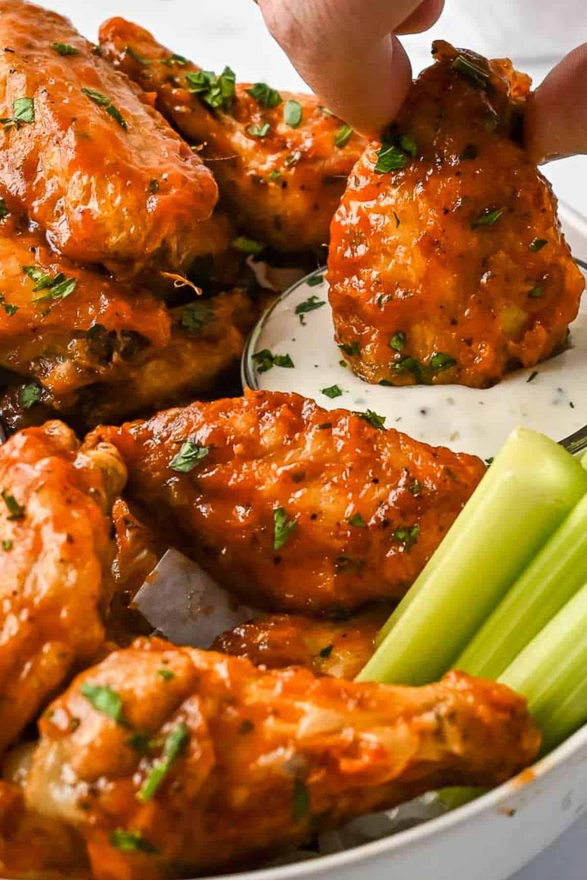 wings in a bowl with celery, one wing dipping into ranch dressing.