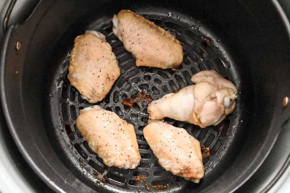 chicken wings cooking in a black air fryer basket.