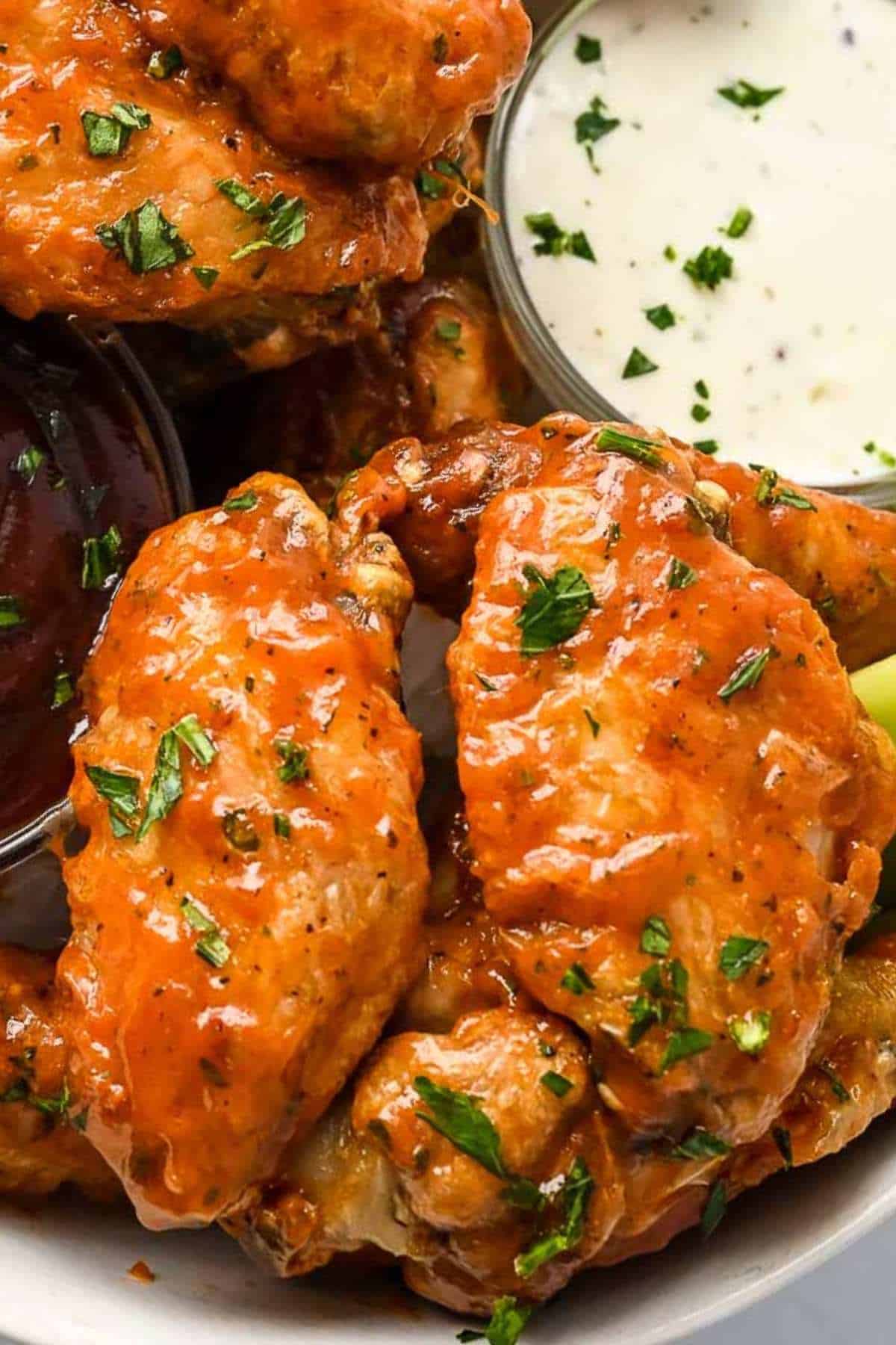 close up of two chicken wings with buffalo sauce and topped with parsley next to ranch dressing.