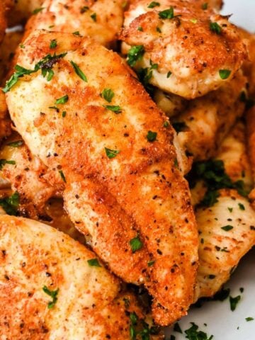 close up shot of air fryer chicken tenders with no breading topped with parsley.