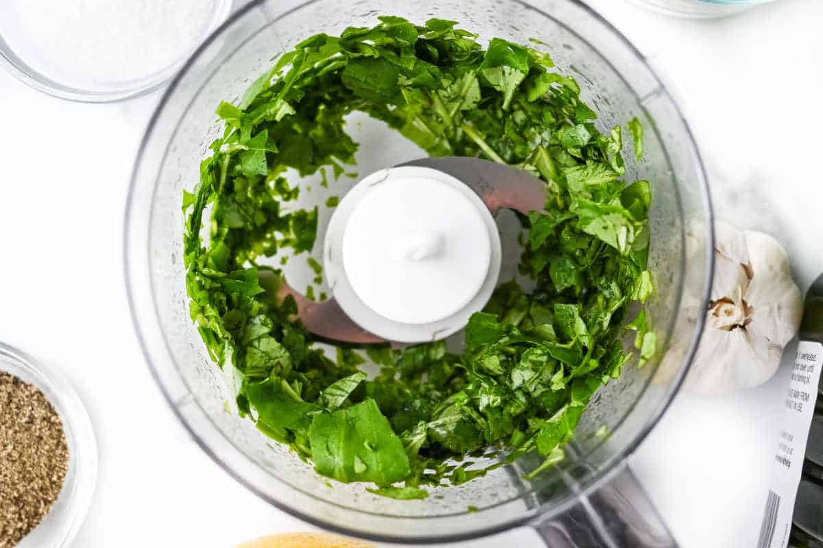 top down view of basil in a food processor on a white background.