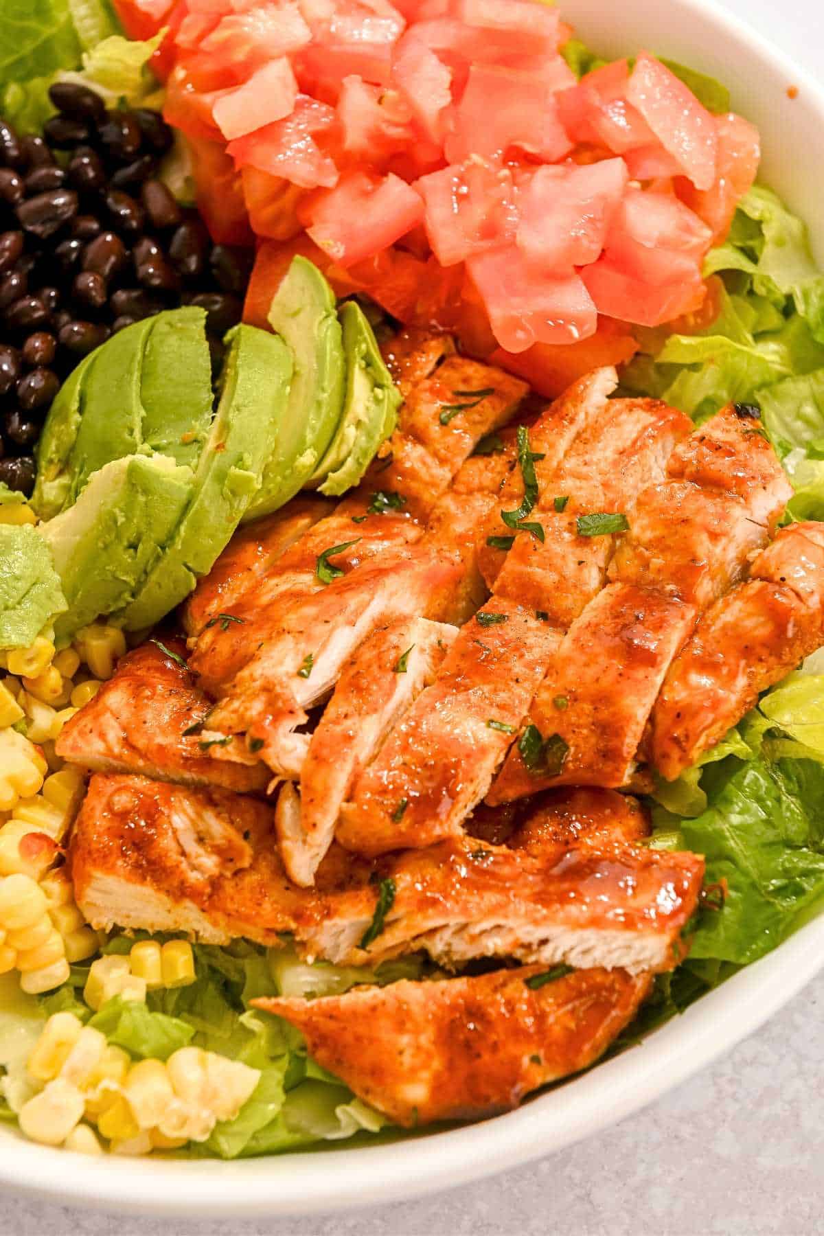 air fryer bbq chicken breast on top of lettuce with corn, tomatoes, avocado, and black beans.