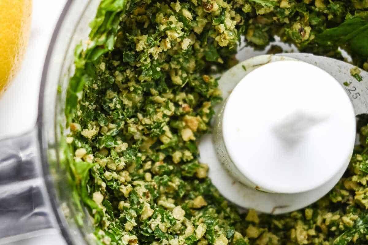 close up shot of chopped up basil pesto ingredients in a food processor.
