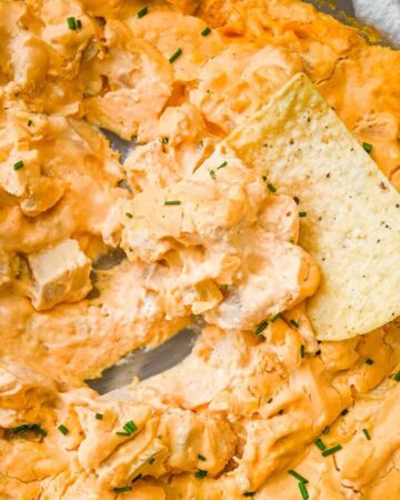 close up shot of buffalo chicken dip with a chip scooping it out.