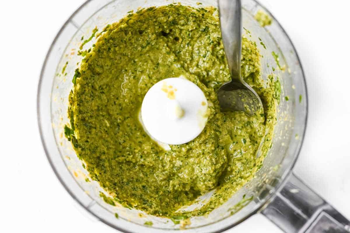 fresh pesto in a food processor with a spoon on a white background.