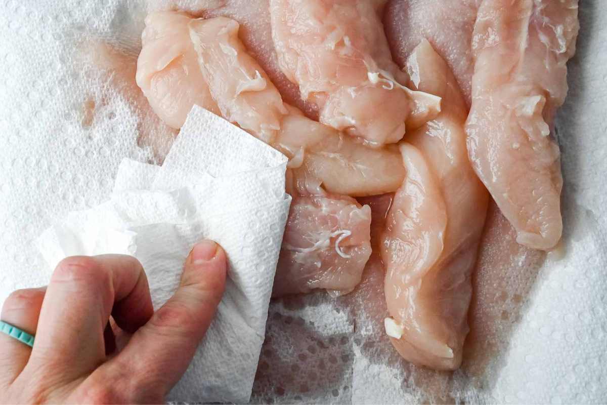 view of hand blotting raw chicken tenders with a paper towel.