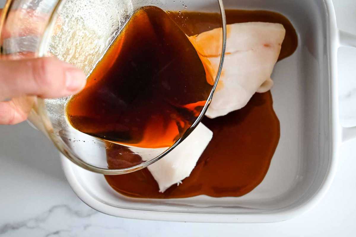 pouring soy marinade over chilean sea bass in a white dish.