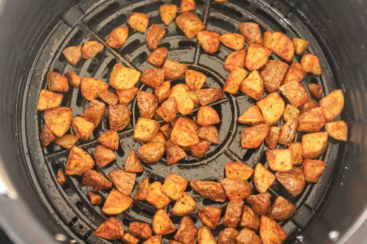 close up shot of breakfast potatoes in a black air fryer basket.