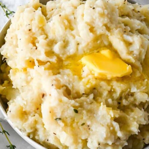 closeup of mashed potatoes and cauliflower topped with butter.