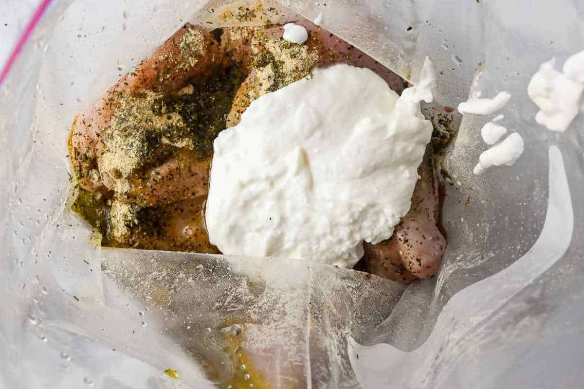 Greek yogurt on top of seasoned chicken in a ziploc bag.