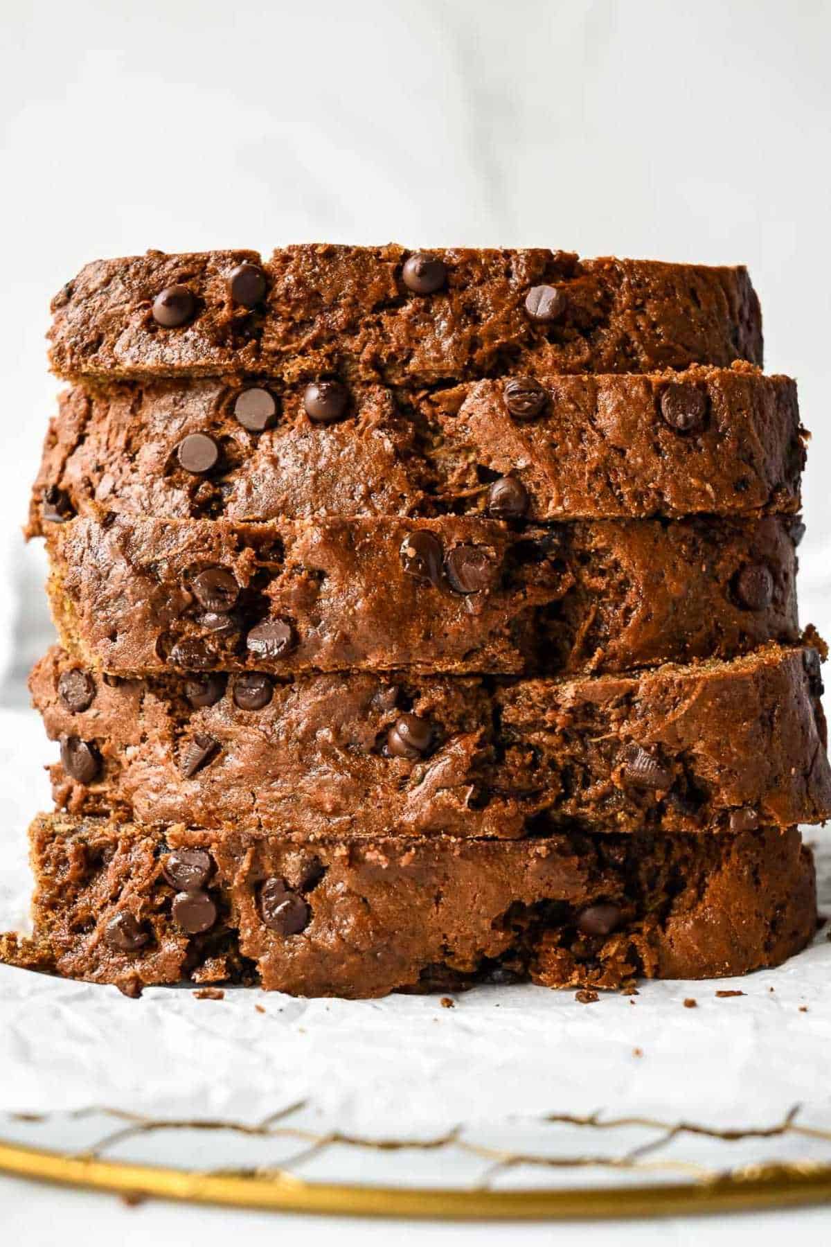 slices of healthy zucchini bread with applesauce on a piece of parchment paper and a gold dish.