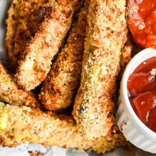 close up of zucchini sticks with breading with dipping sauces on the side.