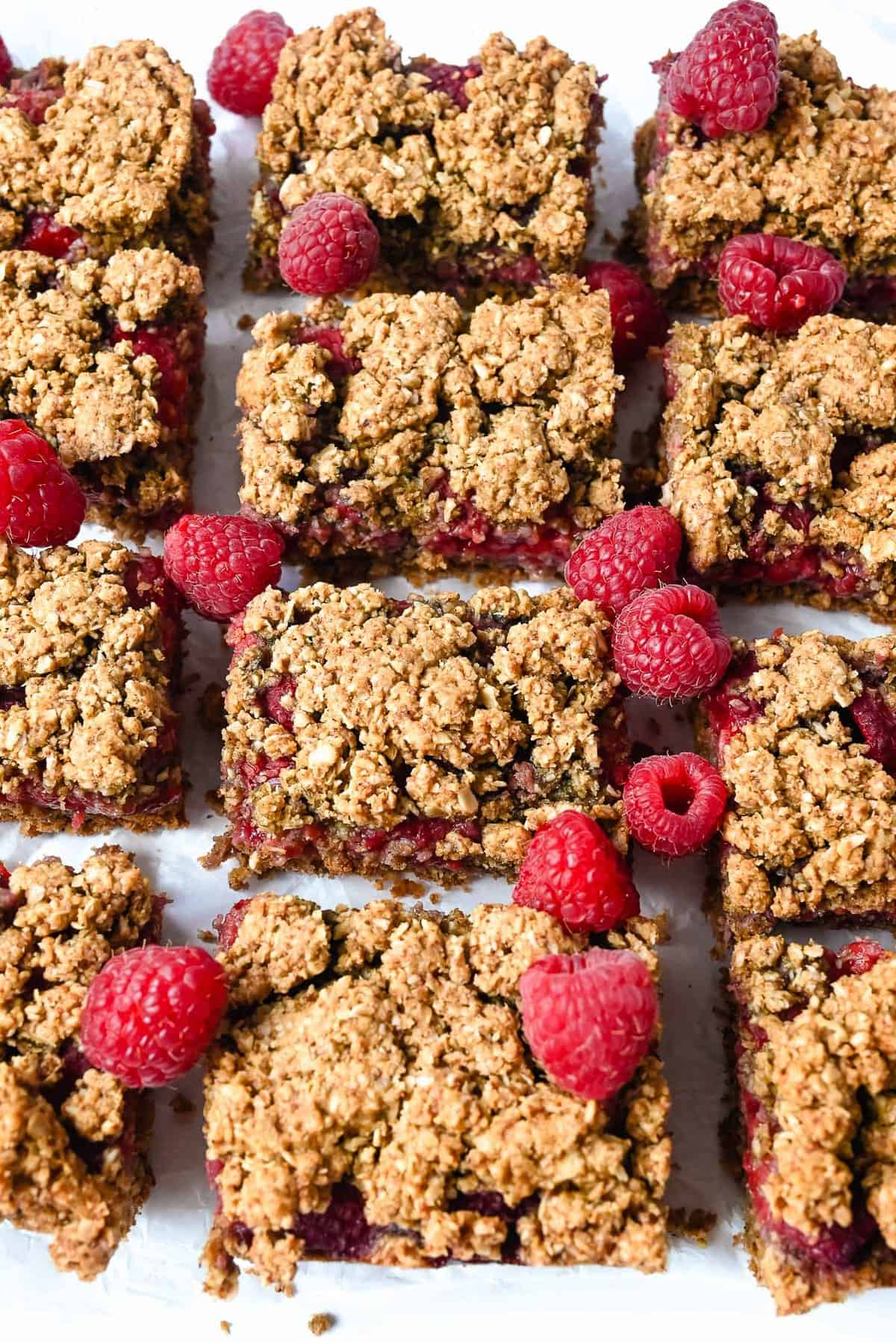 cut up bars topped with raspberries laying on a white surface.