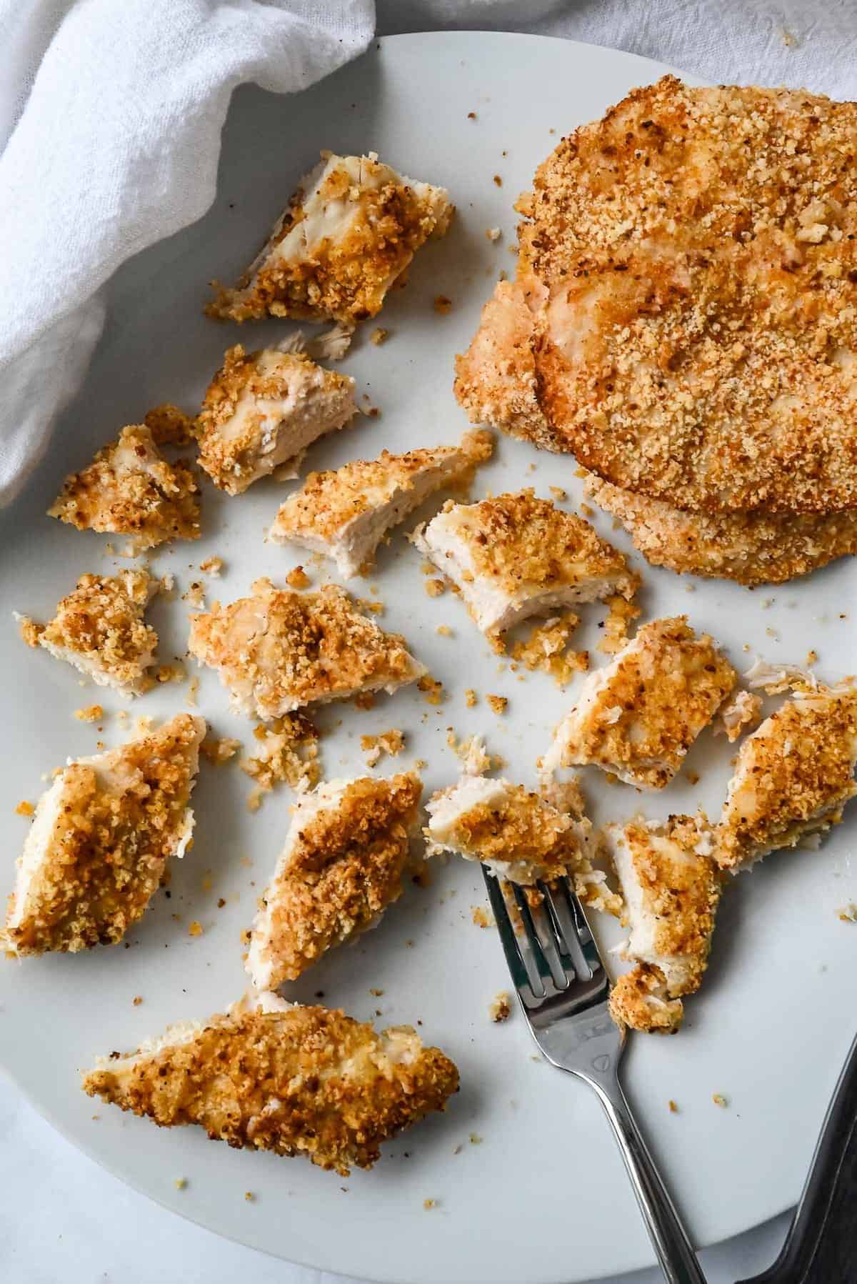 small cut pieces of panko chicken on a white plate with a fork.