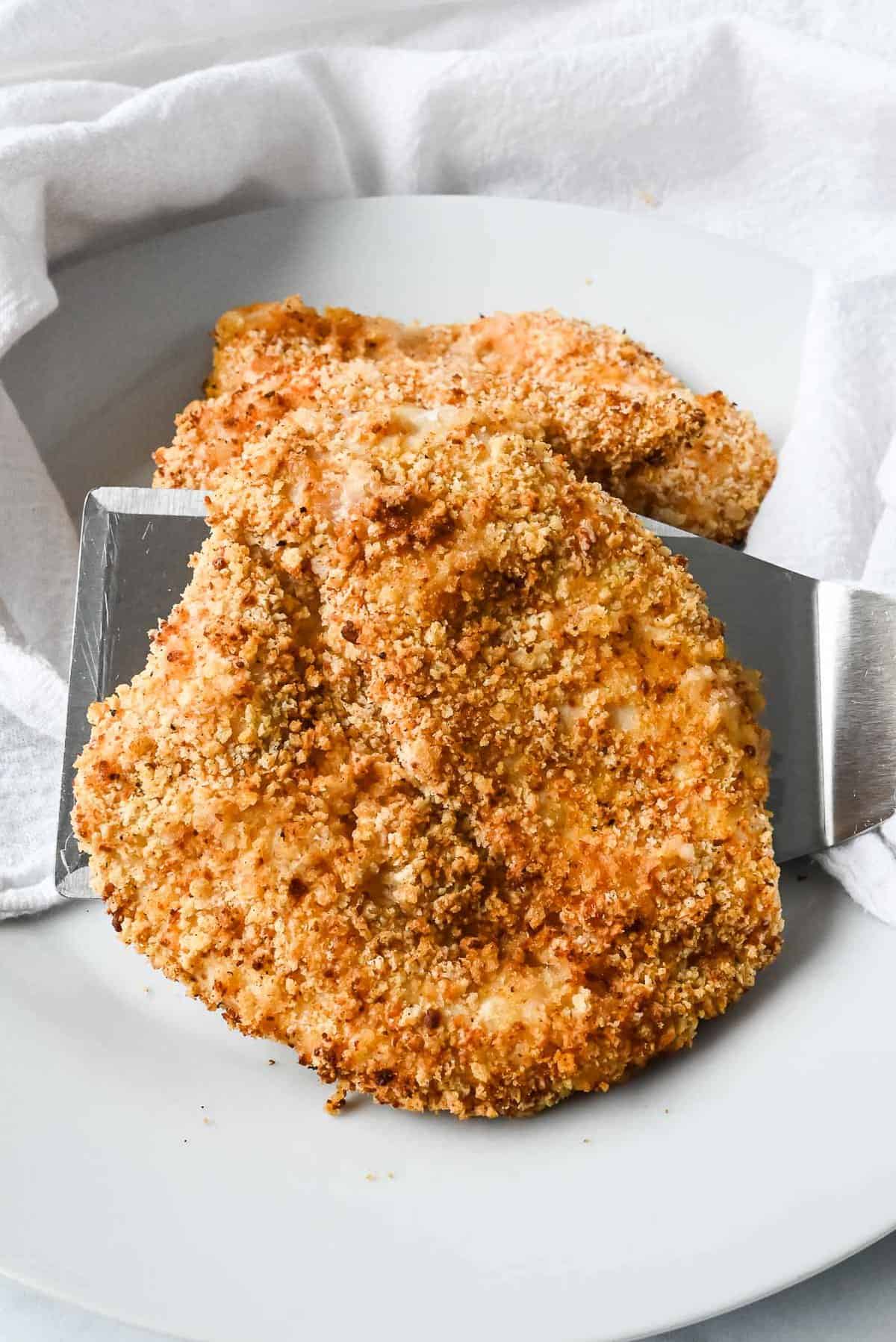 plate of crispy panko chicken on a spatula and a white plate.