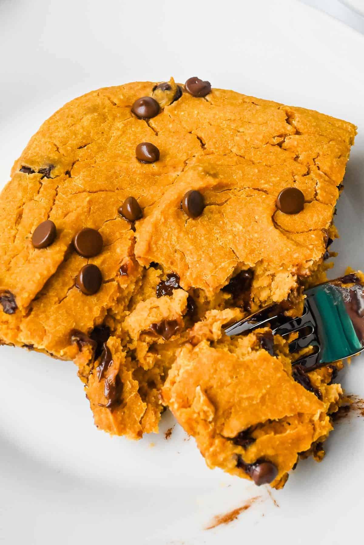 slice of pumpkin baked oatmeal with chocolate chips on a white plate with a fork holding a piece.