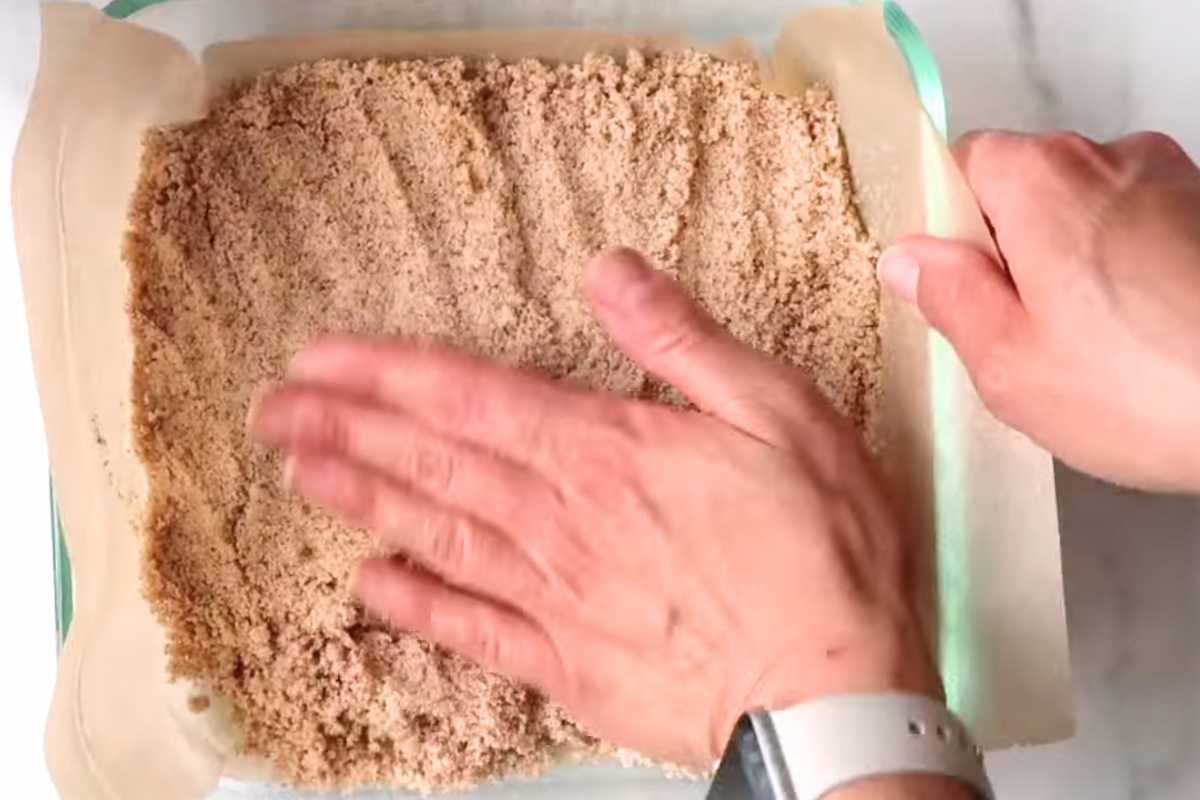 hand pressing crust ingredients into a glass dish.
