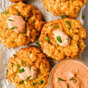 healthy air fryer crab cakes on white parchment paper topped with remoulade sauce and green onions.