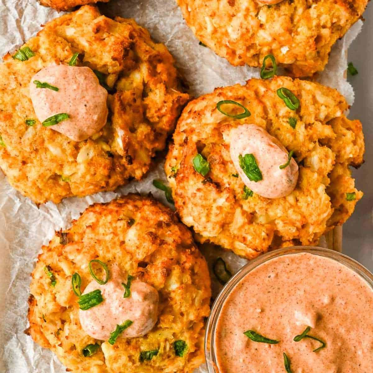 healthy air fryer crab cakes on white parchment paper topped with remoulade sauce and green onions.