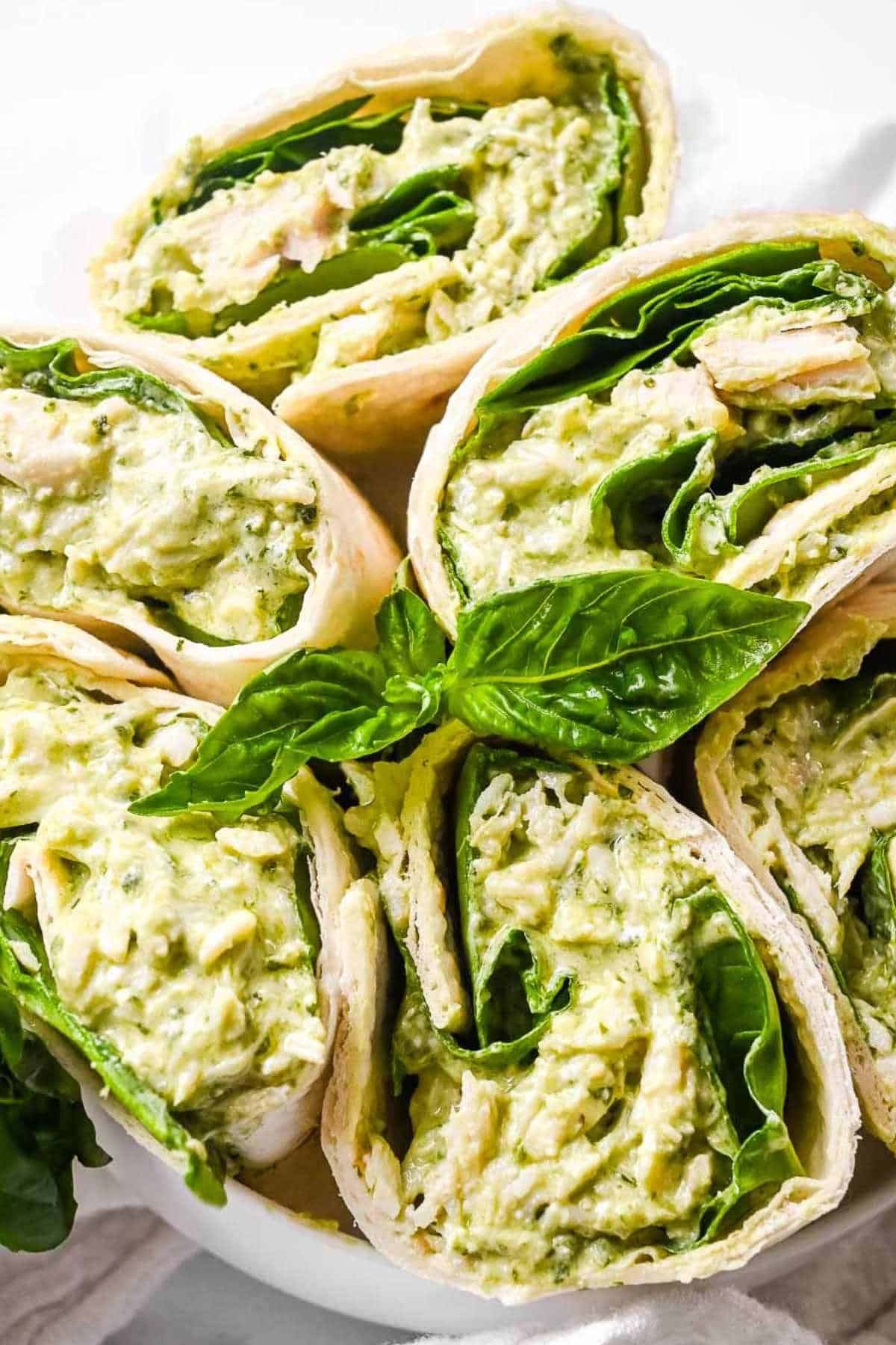 pesto chicken salad in wraps with basil on top.