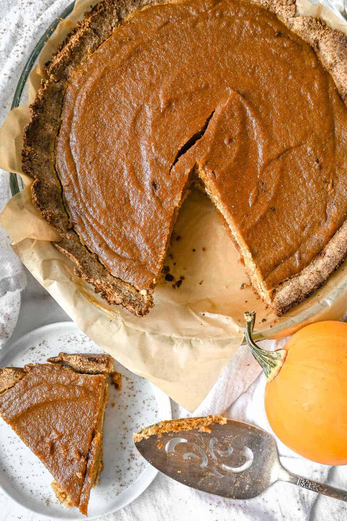 full pumpkin pie with one slice on a small white plate.
