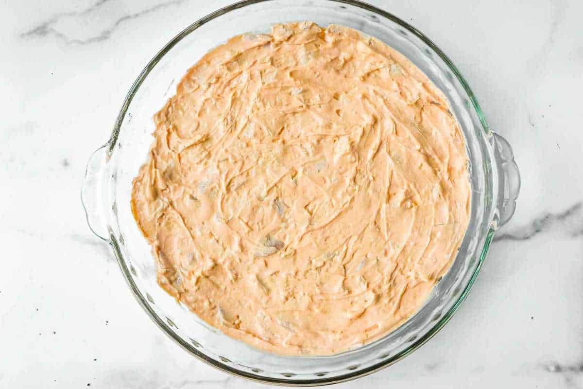 buffalo chicken dip ingredients in a glass pie plate on a white marble background.
