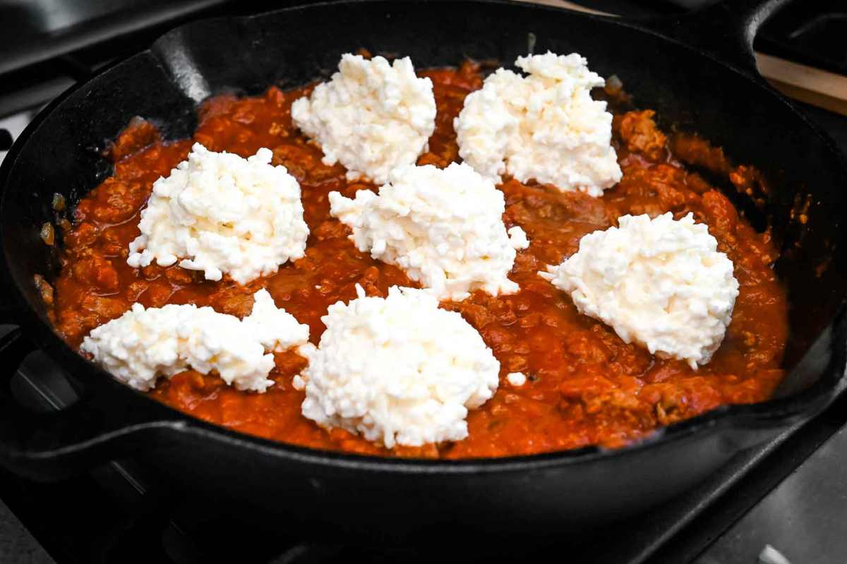 scoops of cheese on top of meat sauce in a cast iron skillet.