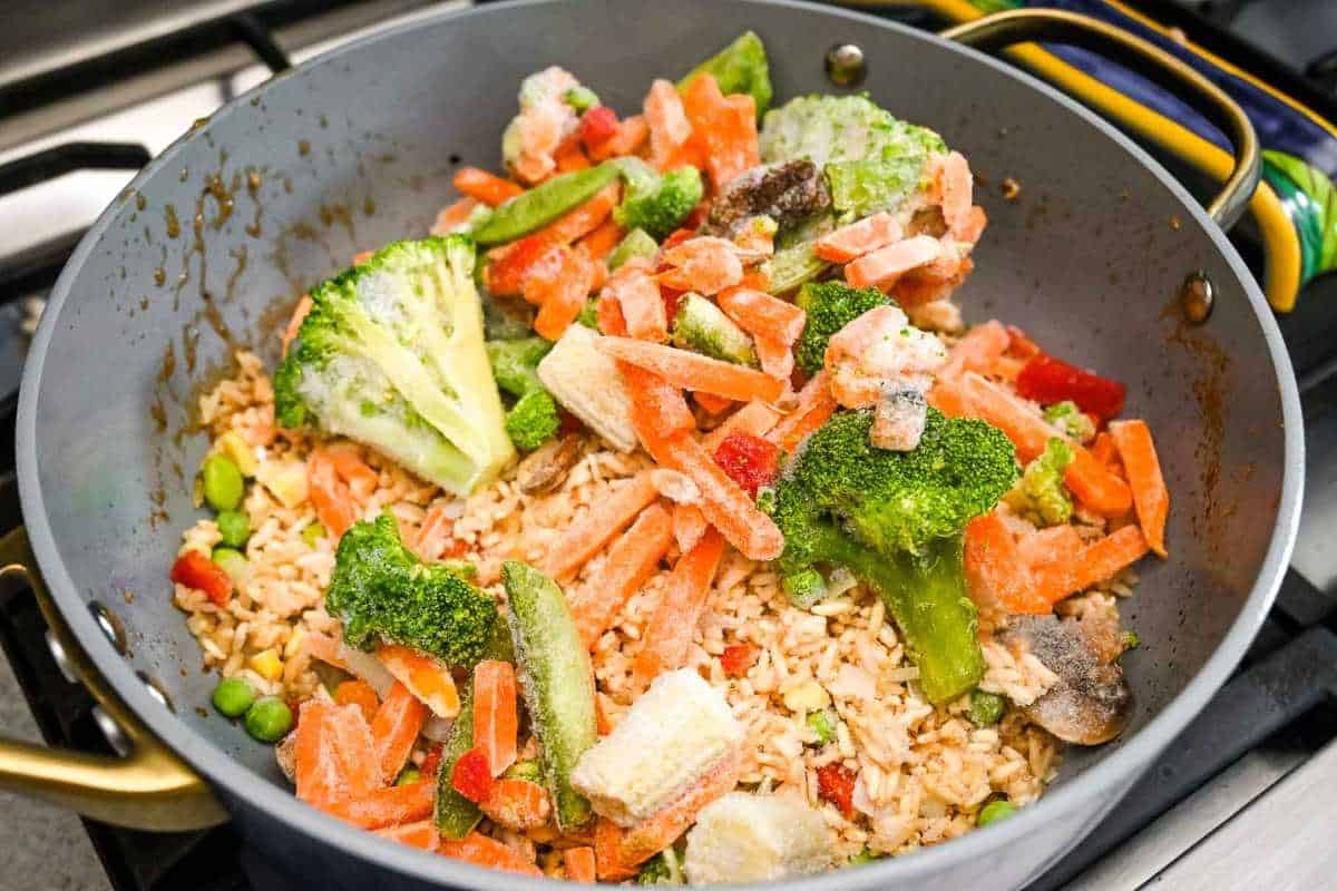 fried rice and frozen vegetables in a gray skillet on the stove.