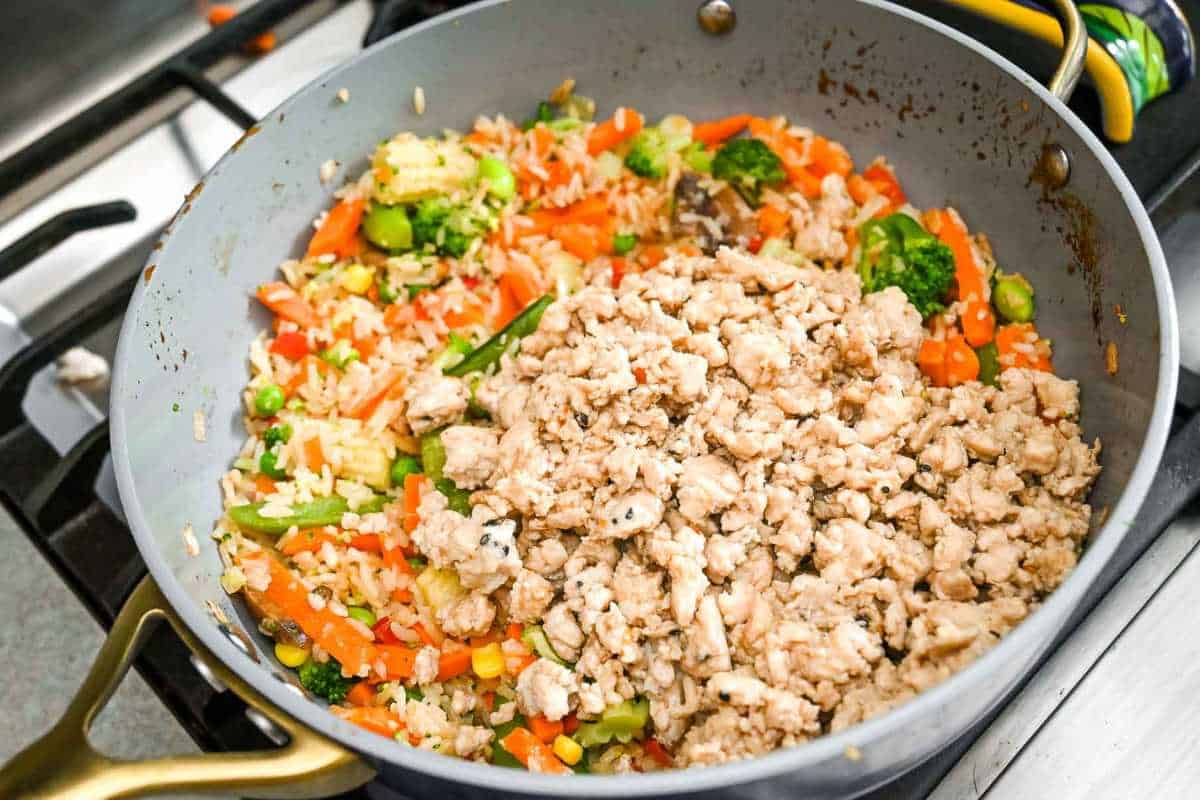 cooked vegetables and ground chicken stir fry in a gray pan on the stove.