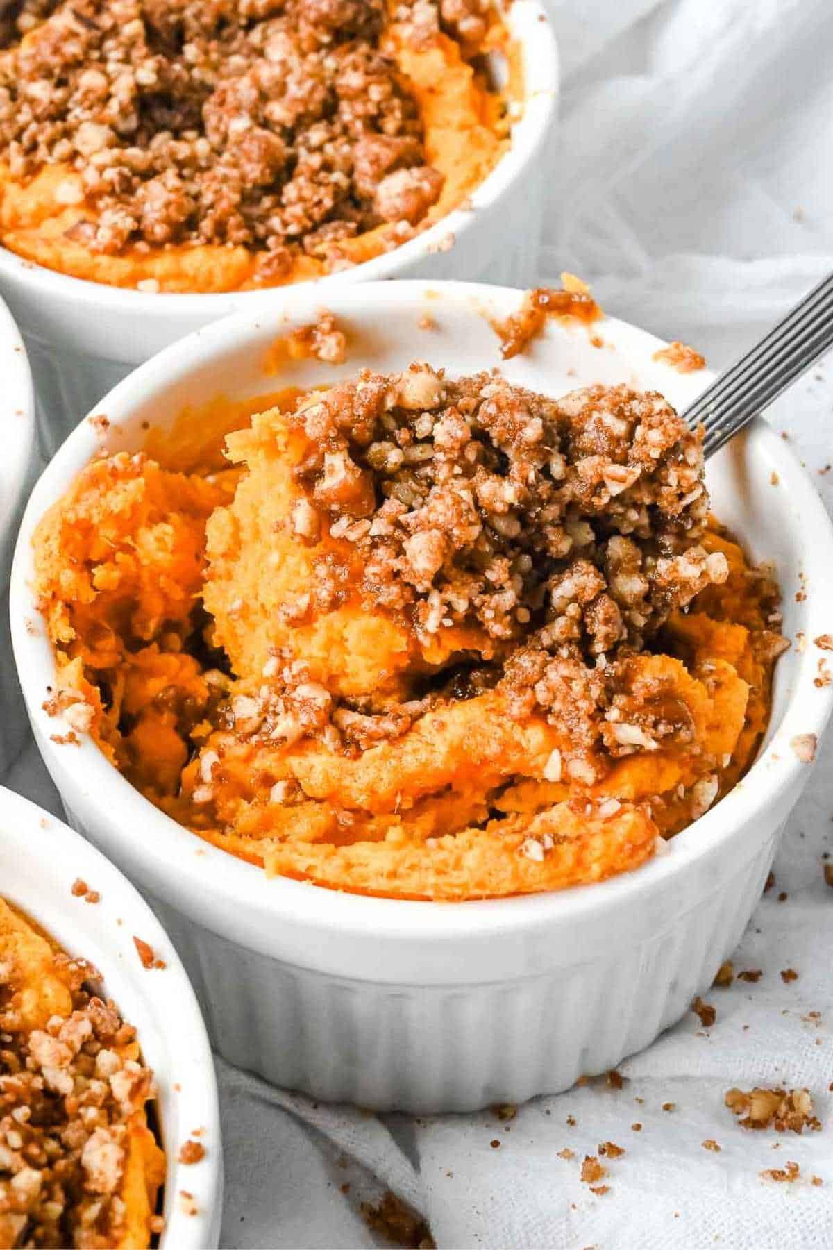 individual ramekin of Ruth's Chris Sweet Potato Casserole topped with pecan crust and a spoon in it.