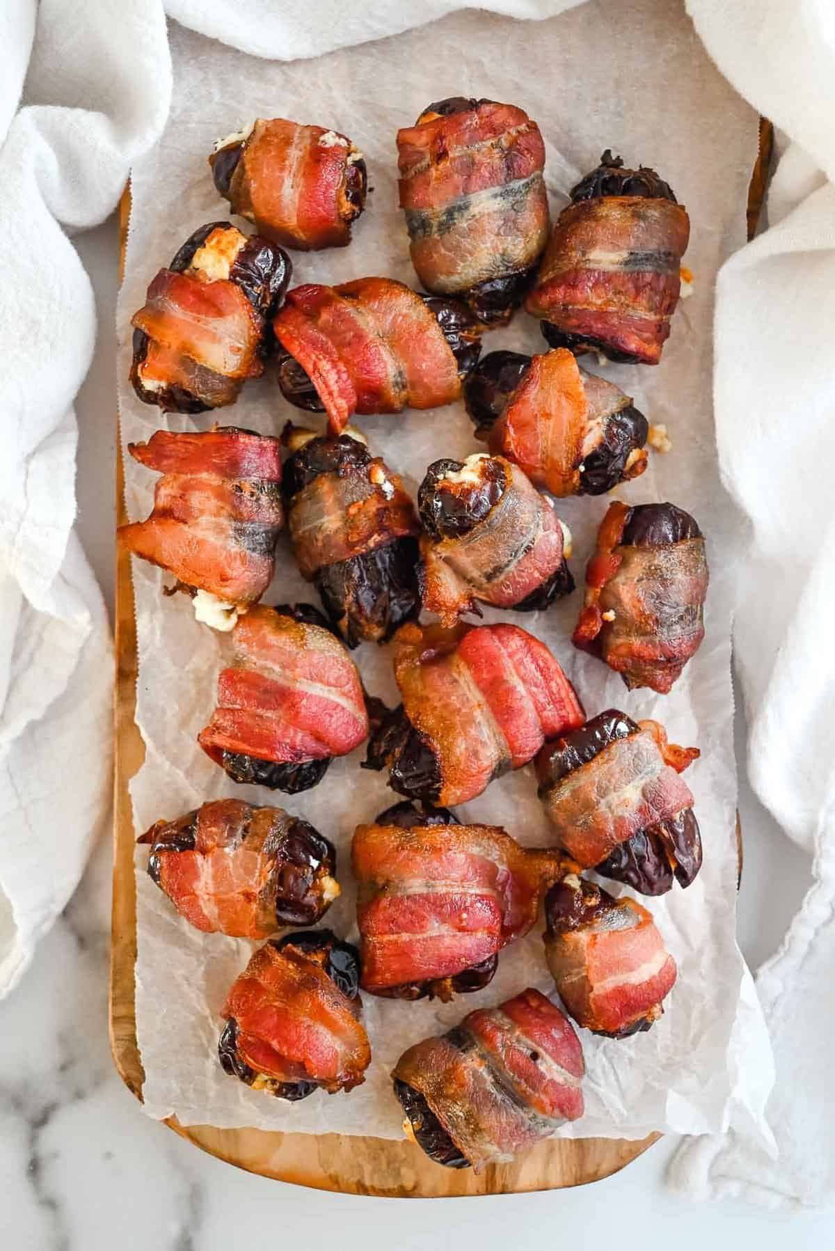 full shot of bacon wrapped goat cheese stuffed dates on white parchment paper.