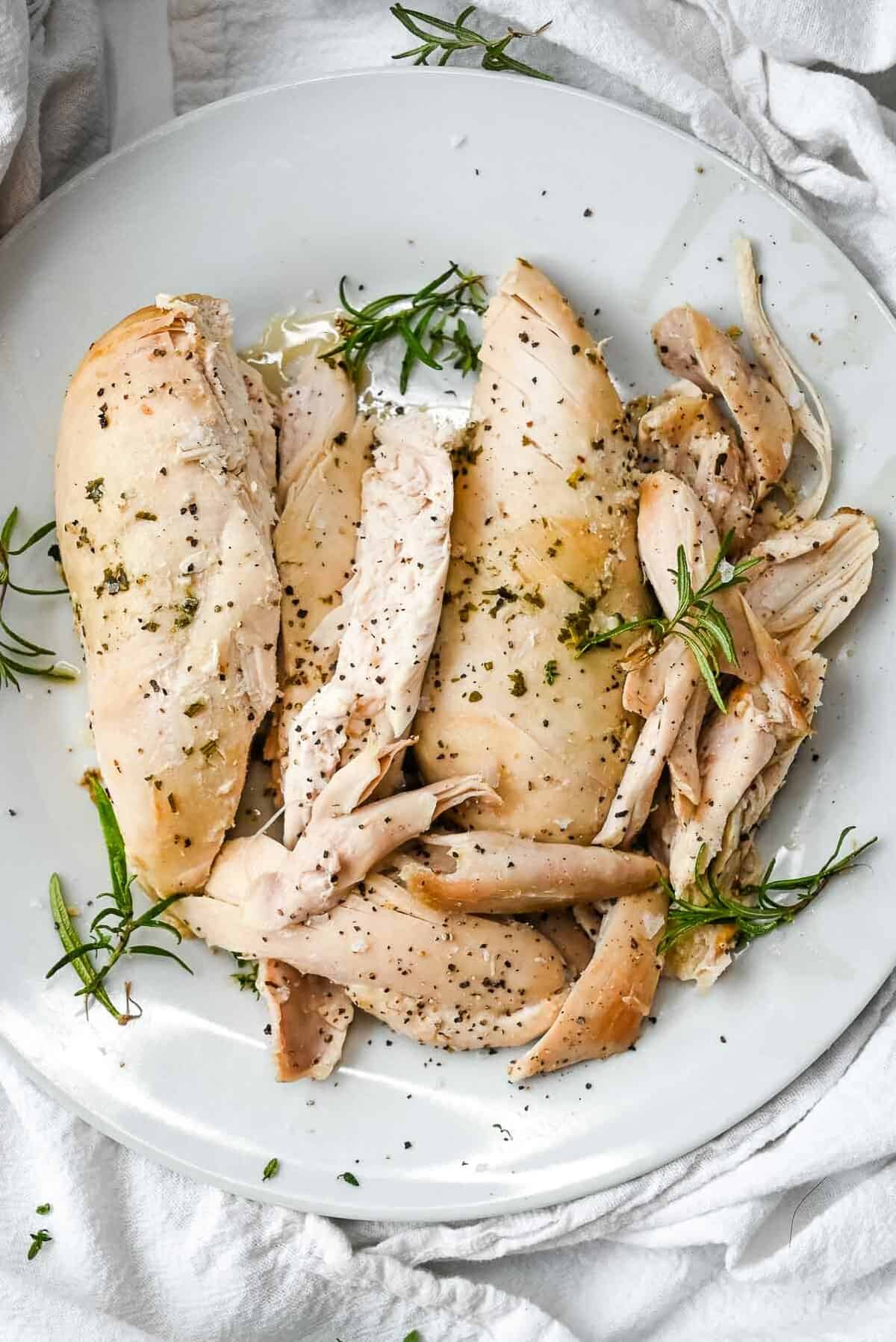 cut chicken meat on a white plate topped with herbs.