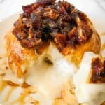 close up of baked brie topped with dates and honey with a piece cut out and gooey cheese running onto the white plate.