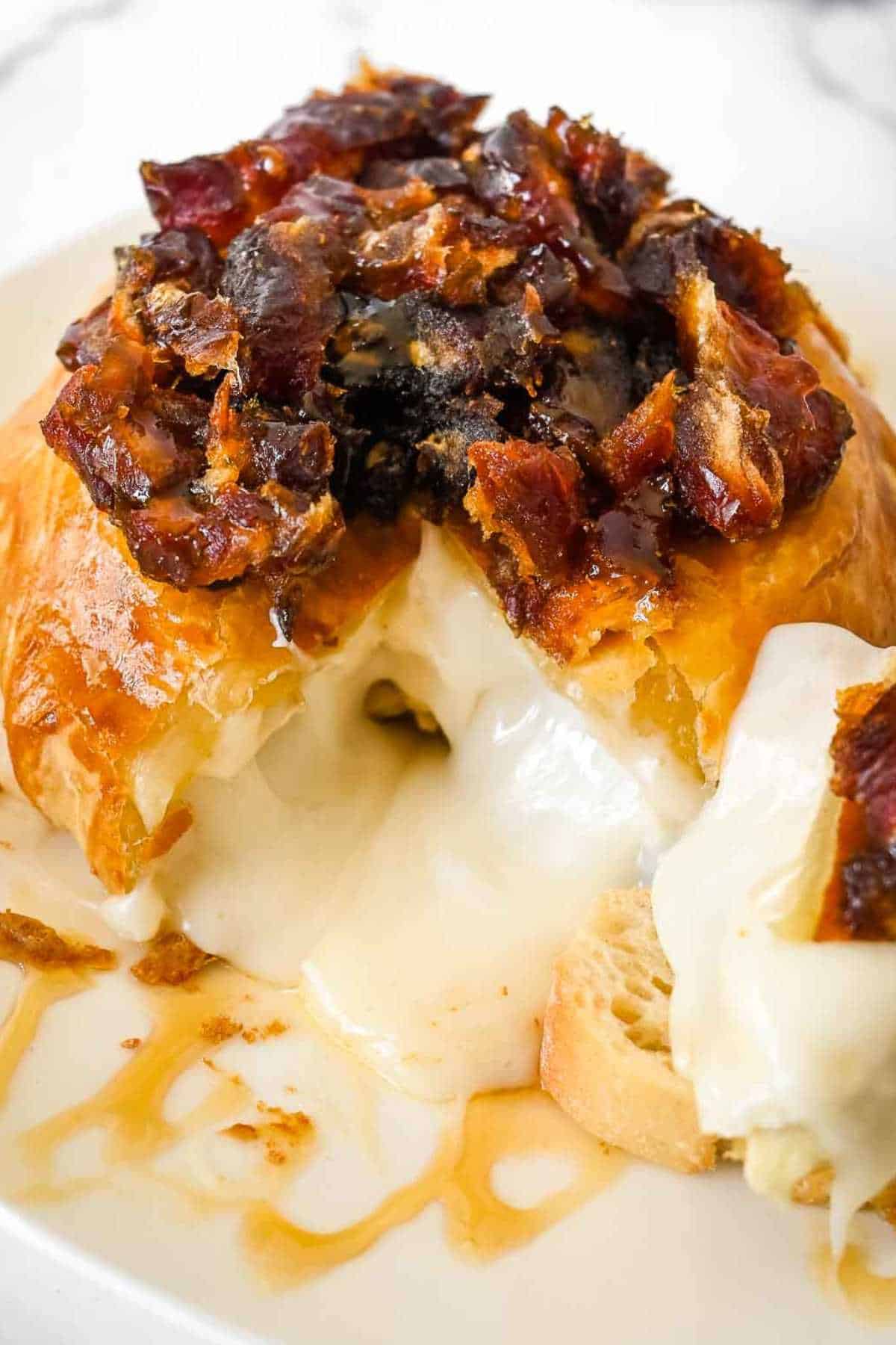 air fryer brie wheel topped with dates and honey with a piece cut out and gooey cheese running onto the white plate.