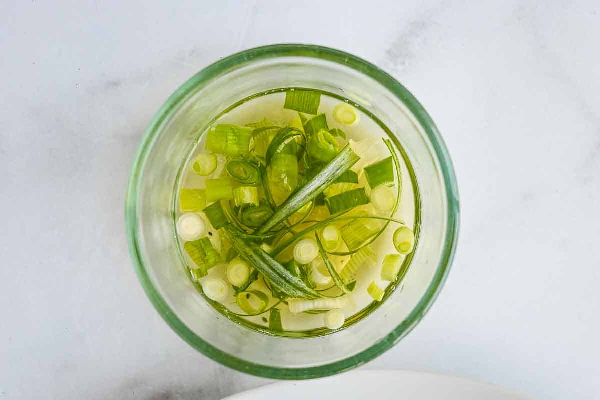 glass bowl of pickled green onions on a white marble background.