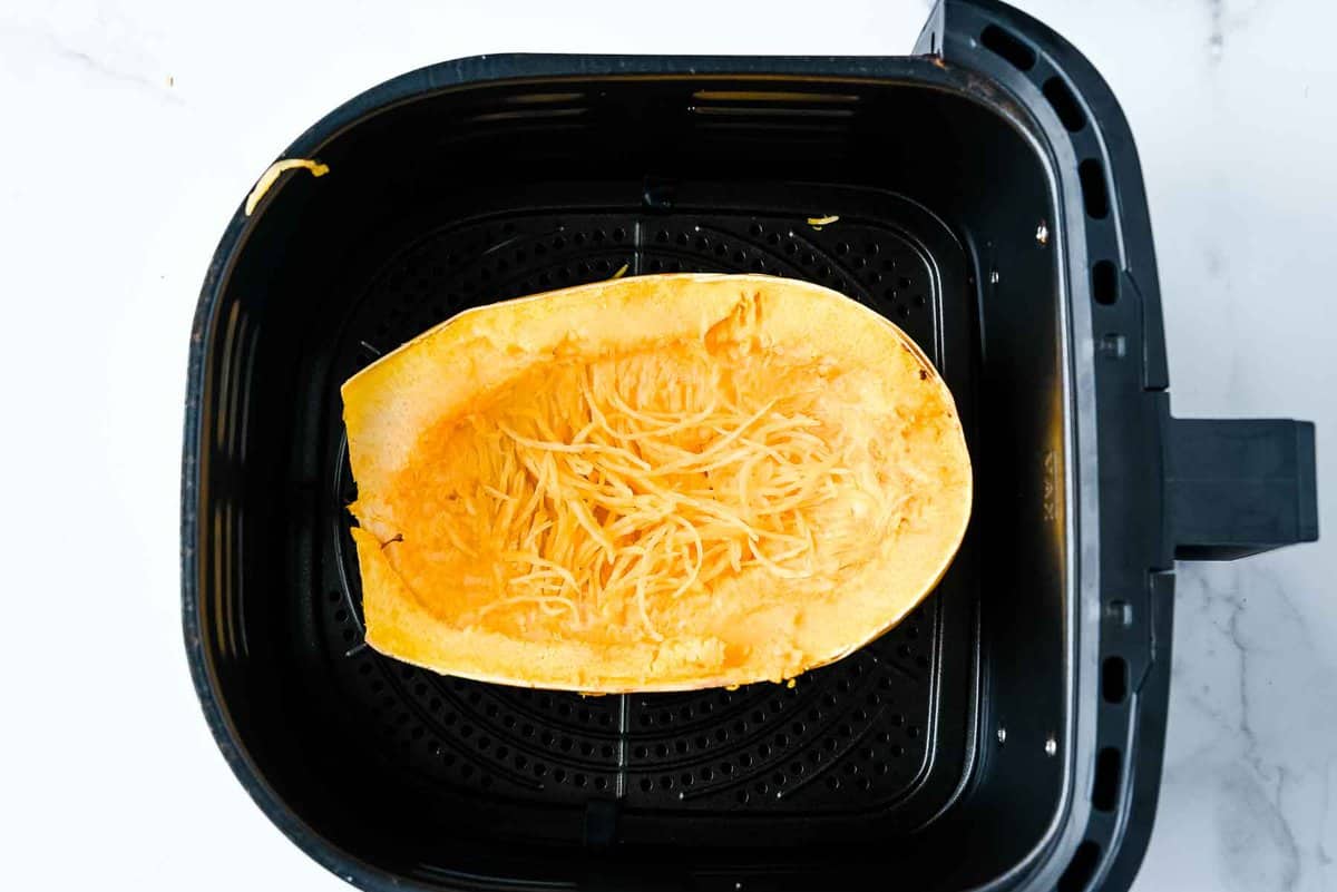cooked air fryer spaghetti squash in a black basket on a white marble background.