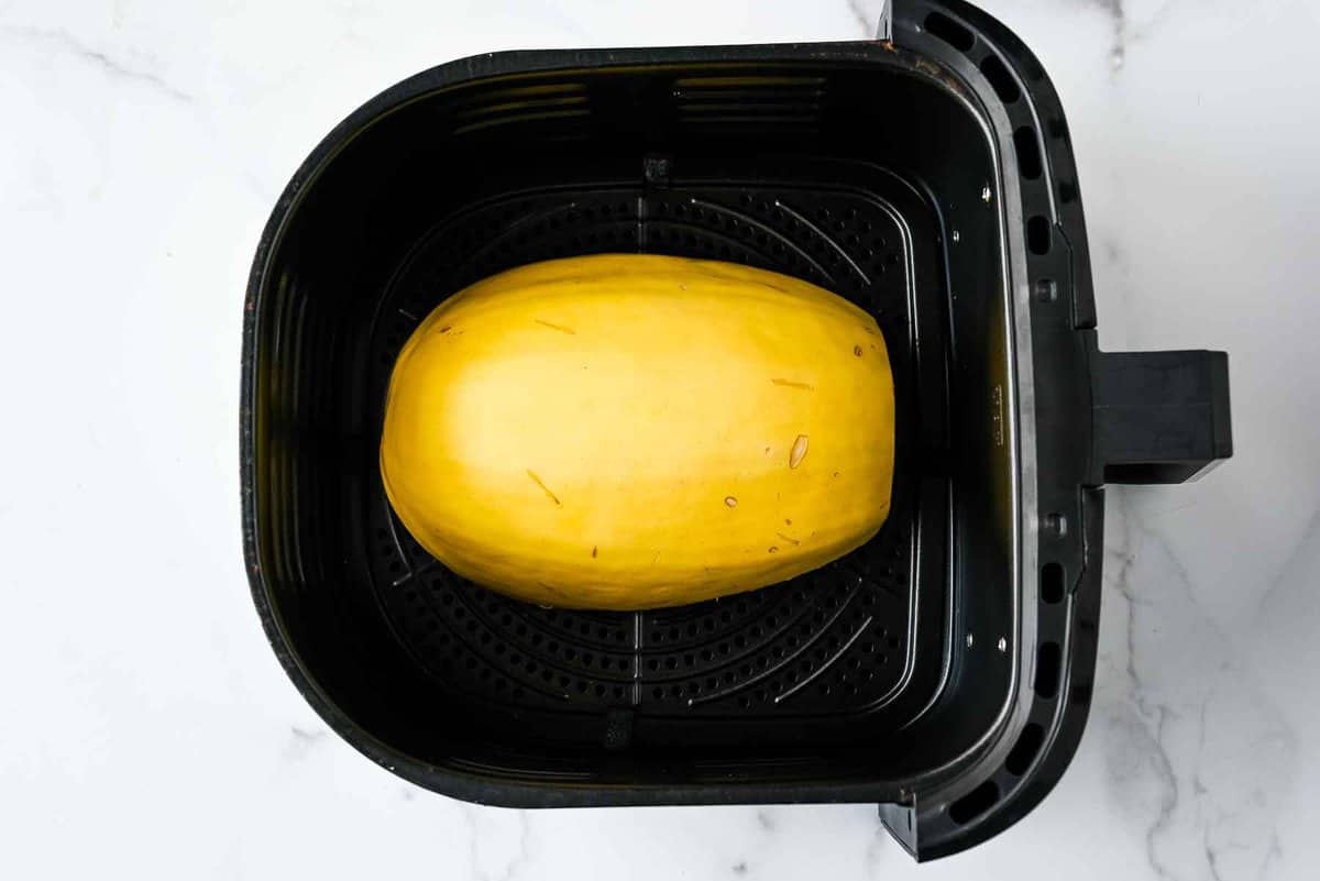 spaghetti squash in a black air fryer basket on a white marble background.