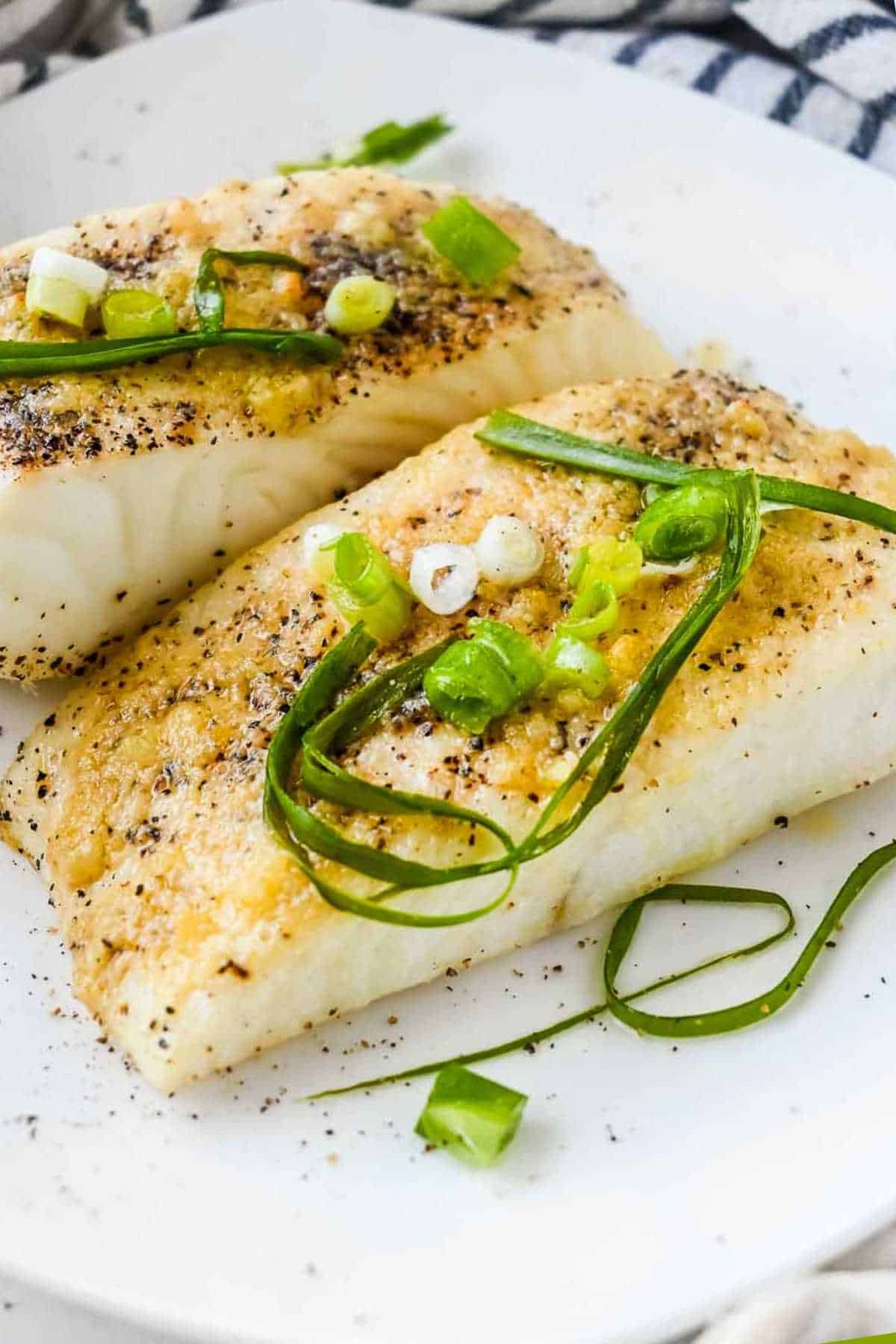 close up of air fryer halibut on a white plate topped with seasoning and green onions on a striped towel.