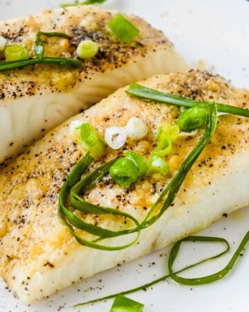 close up shot of air fryer halibut on a white plate topped with green onions and seasoning.