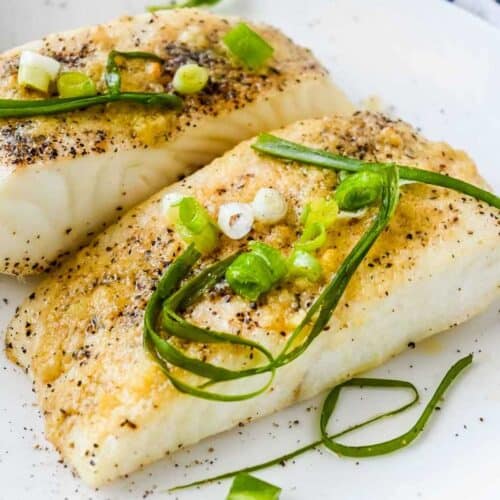 close up shot of air fryer halibut on a white plate topped with green onions and seasoning.