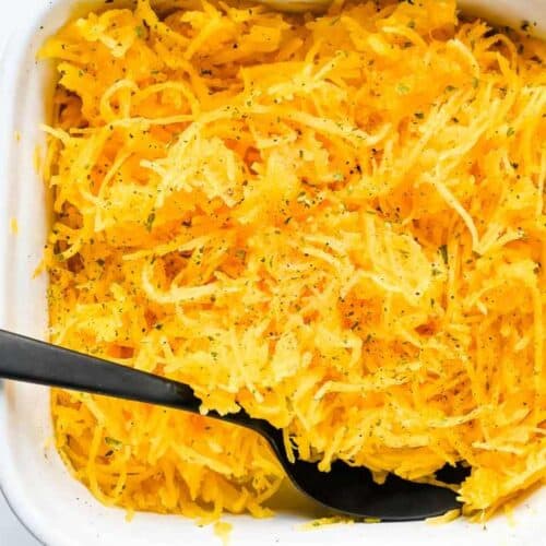 close up shot of air fryer spaghetti squash in a white casserole dish with a black spoon topped with parsley and pepper.