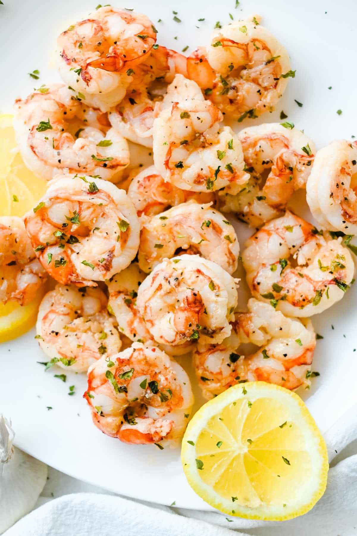 pan seared shrimp on a white plate with lemon and parsley.