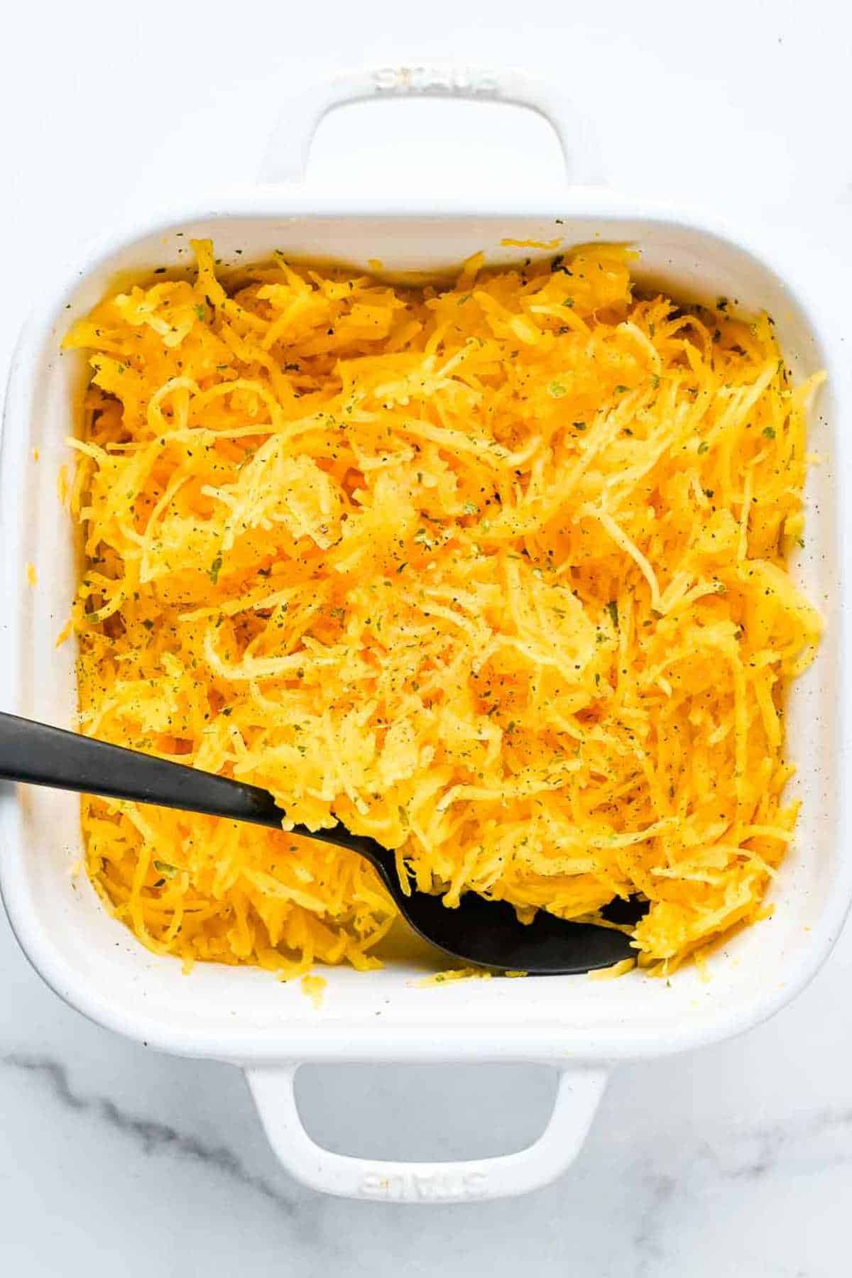 prepared air fryer spaghetti squash in a white casserole dish with a black spoon topped with parsley and pepper.