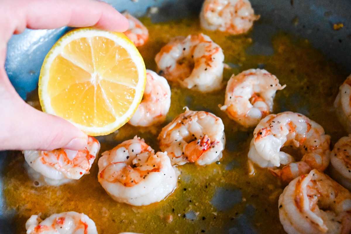 hand putting lemon juice into pan with seared shrimp.
