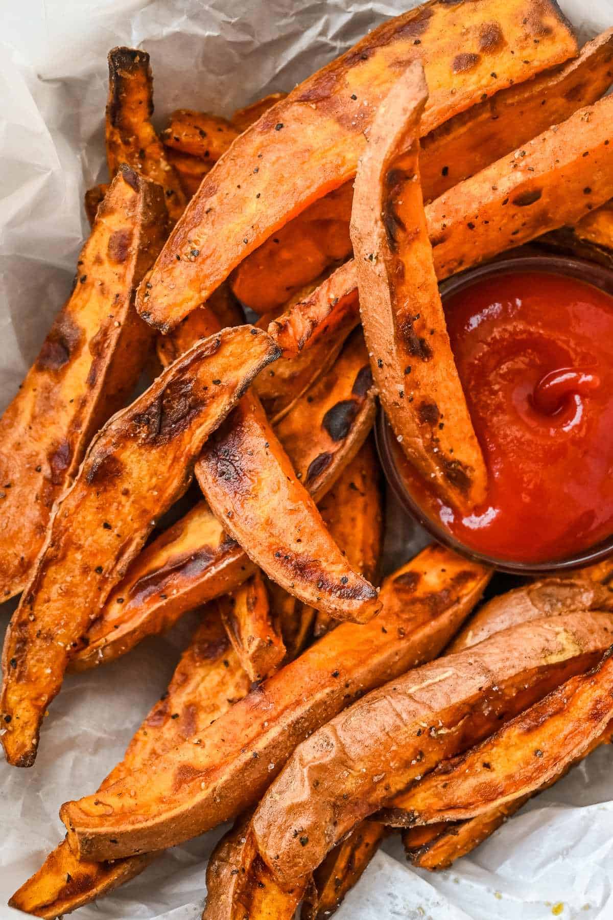 close up of air fryer sweet potato wedges with ketchup on parchment paper.