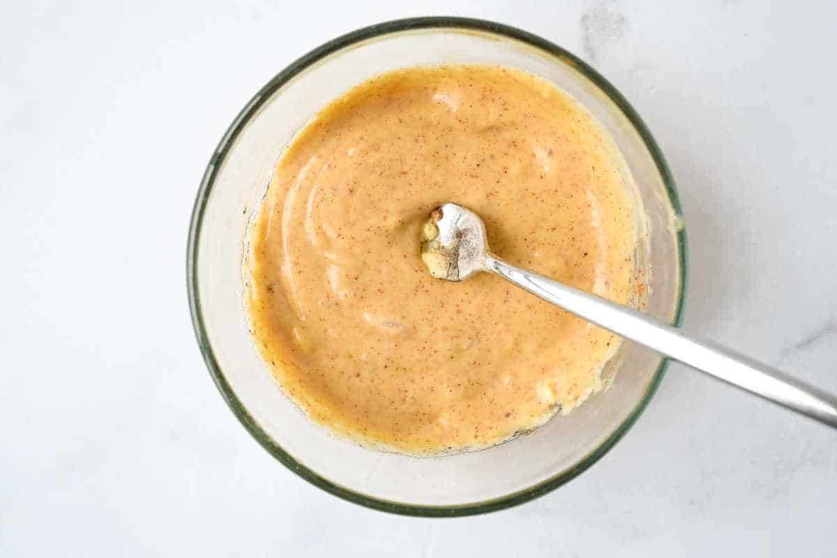 bowl of honey mustard sauce on a white background with a fork in it.
