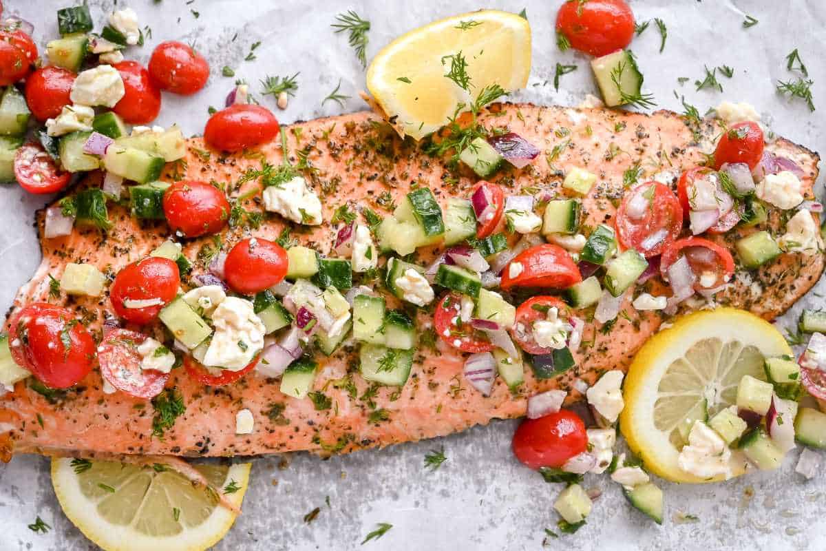 greek salmon topped with lemons and Greek cucumber salad on white parchment paper.