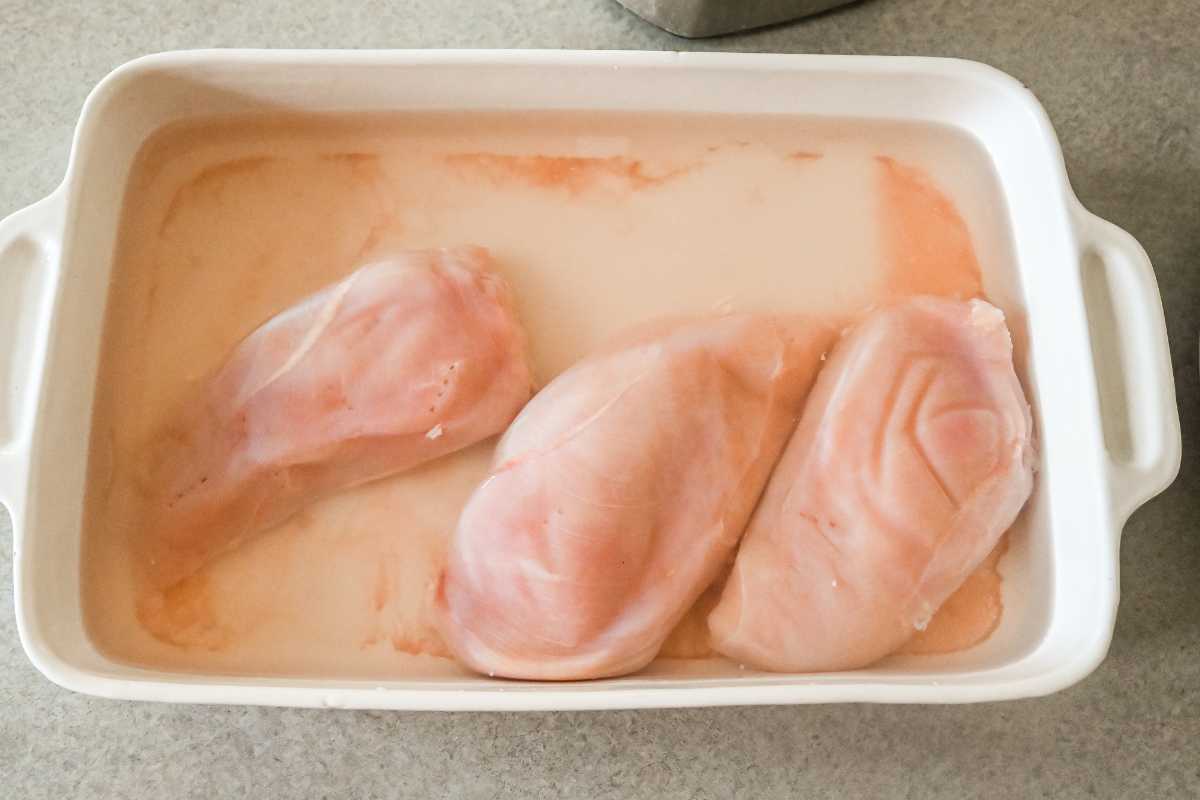 chicken brining in water in a white pan.